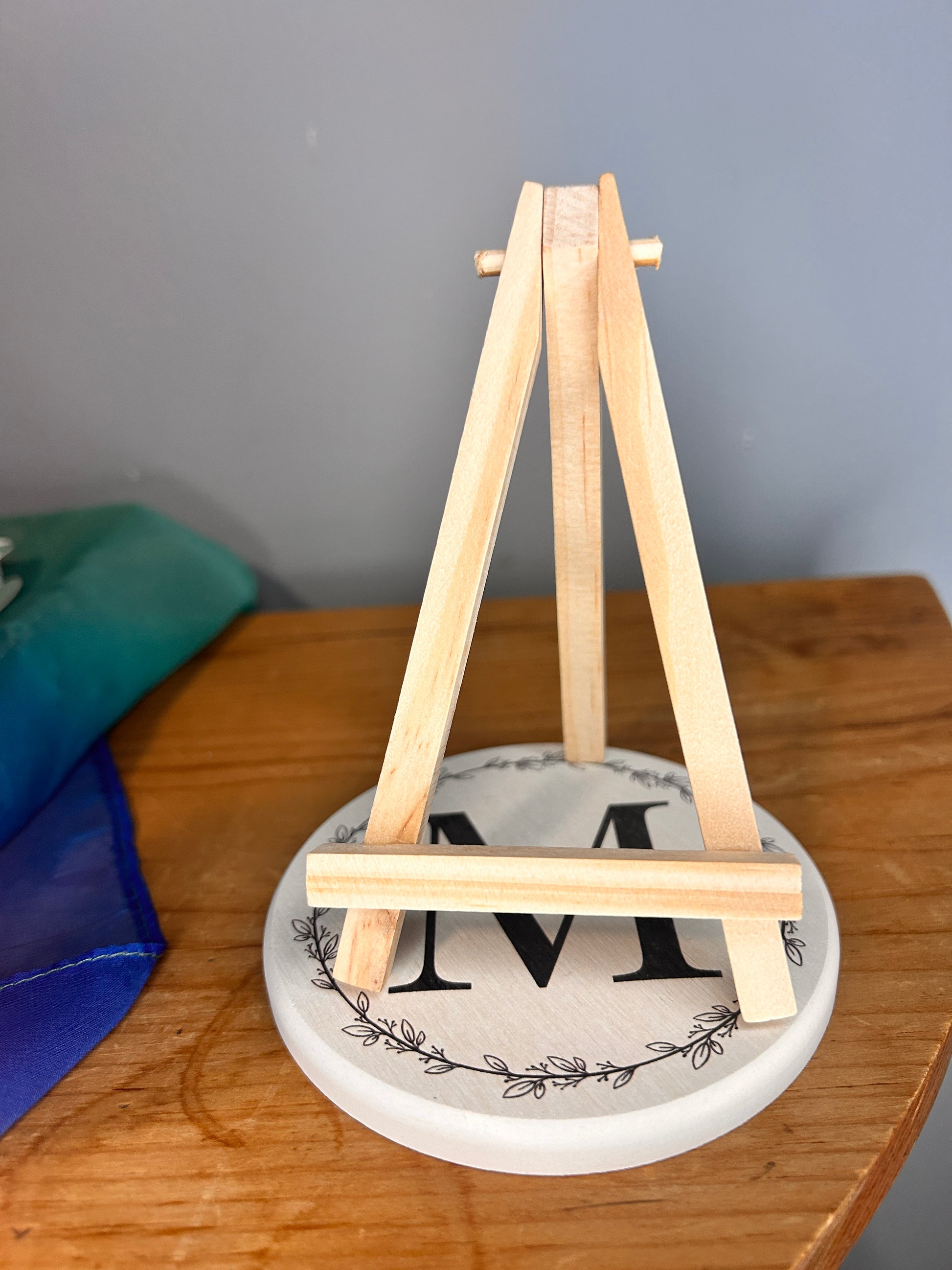 A photo of the wooden miniature easel sitting on a circular white coaster on a wooden dresser or shelf 